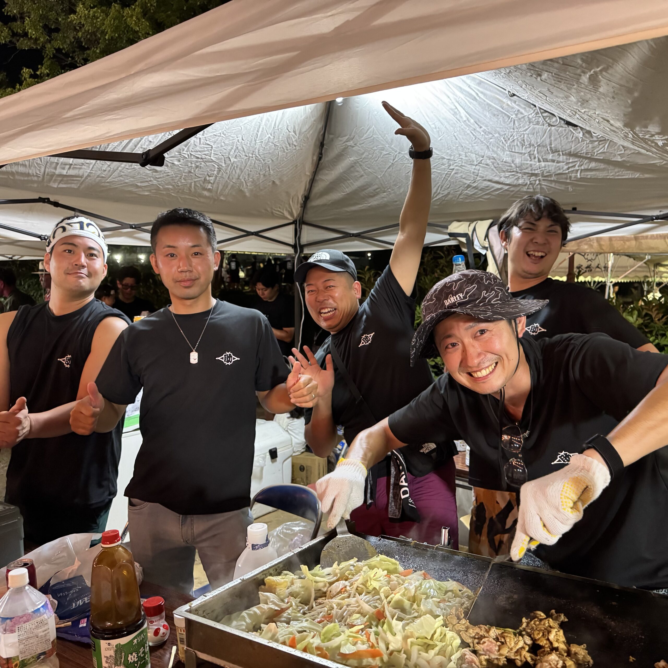鉄板で焼きそばを焼く5人。黒いTシャツに助の印