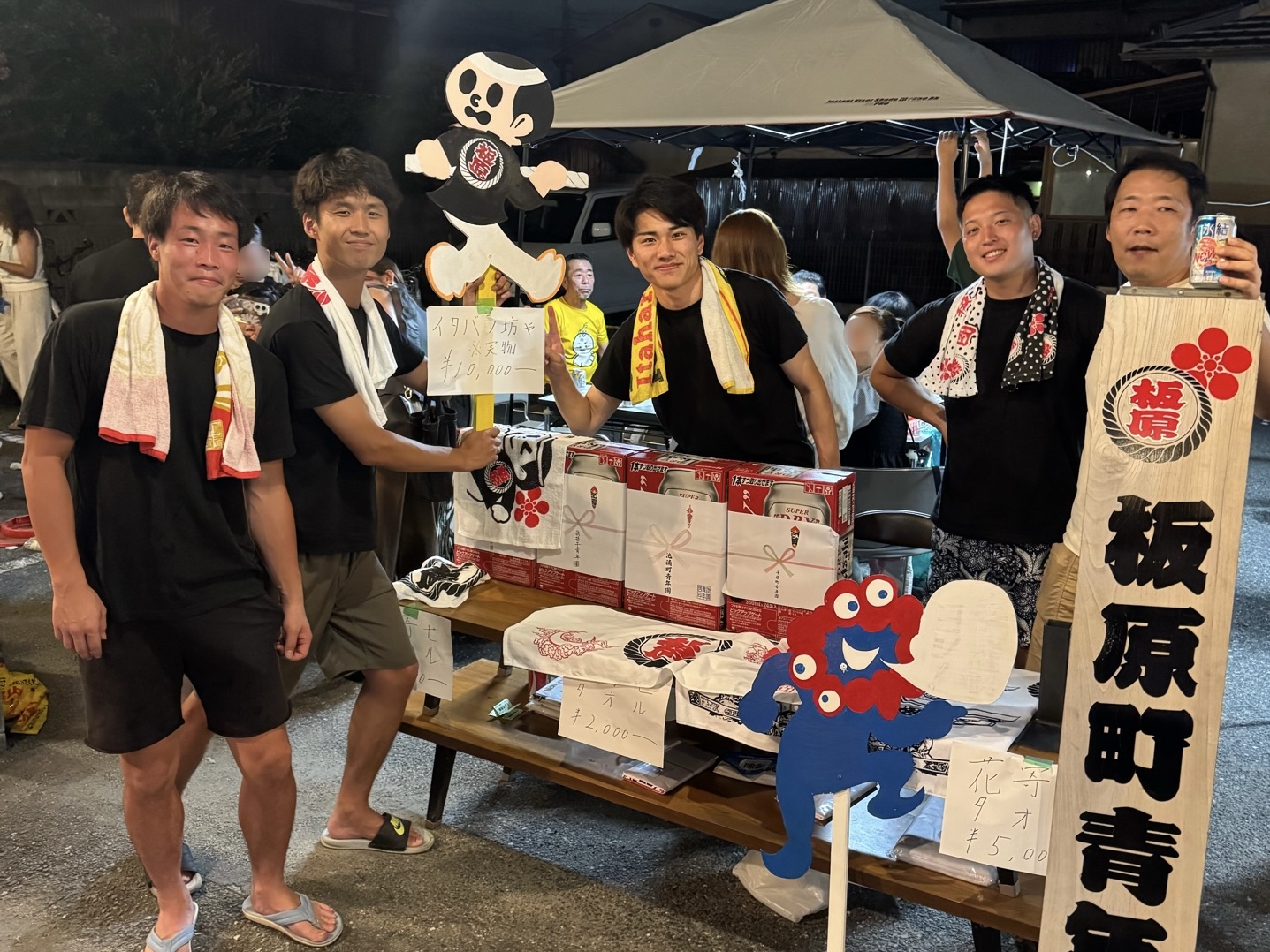 板原町青年團のテント。木の看板を掲げる人と、タオルの並んだテーブル