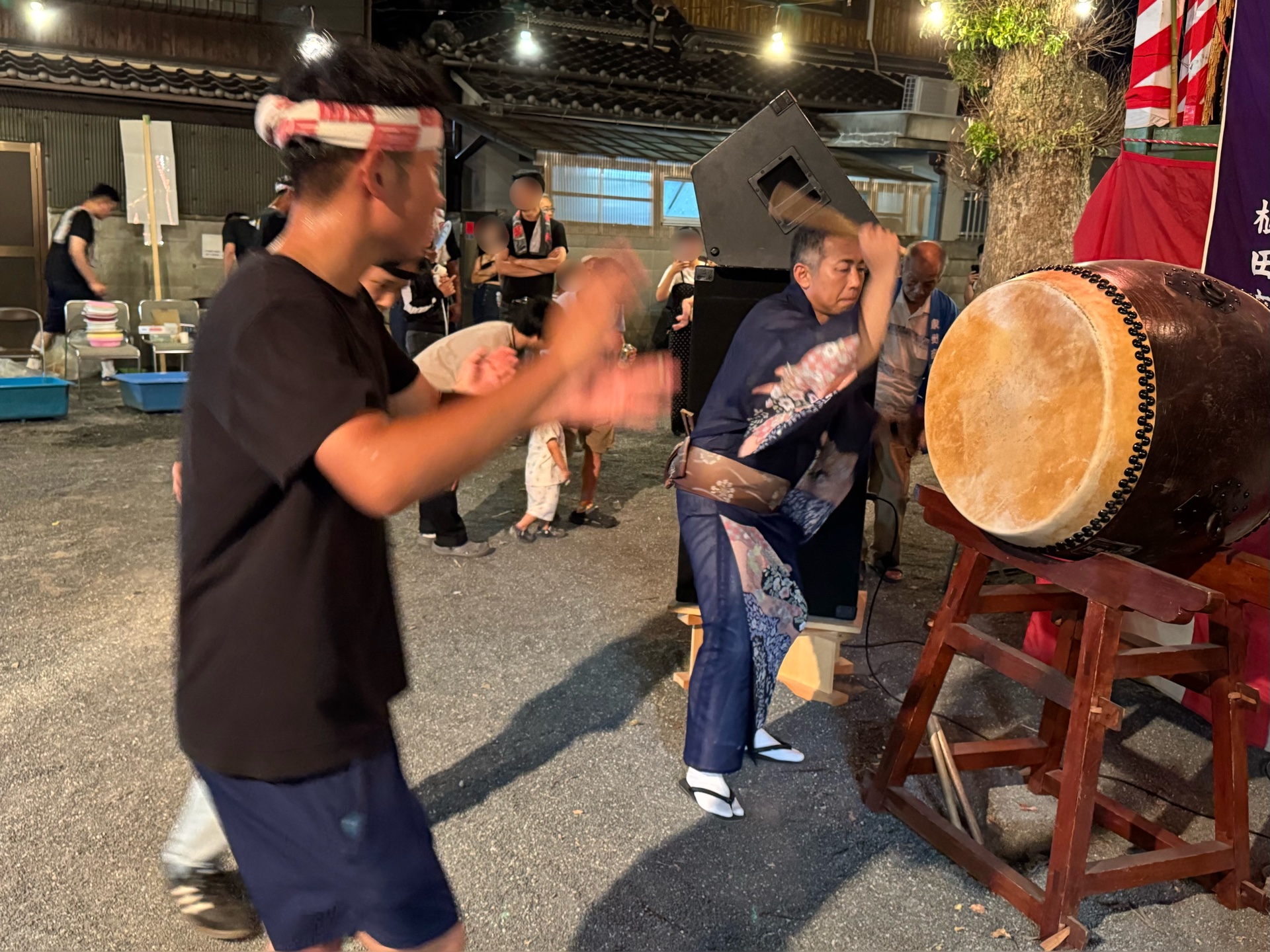 大太鼓を振りかぶって叩く浴衣の男性と、その横で踊る人