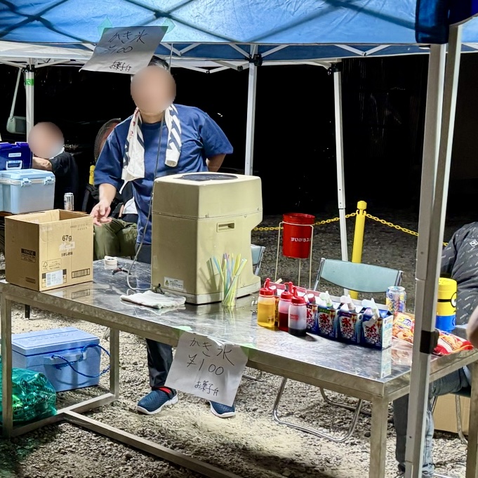 かき氷機とシロップの並ぶ台。手書きの貼り紙が下がる