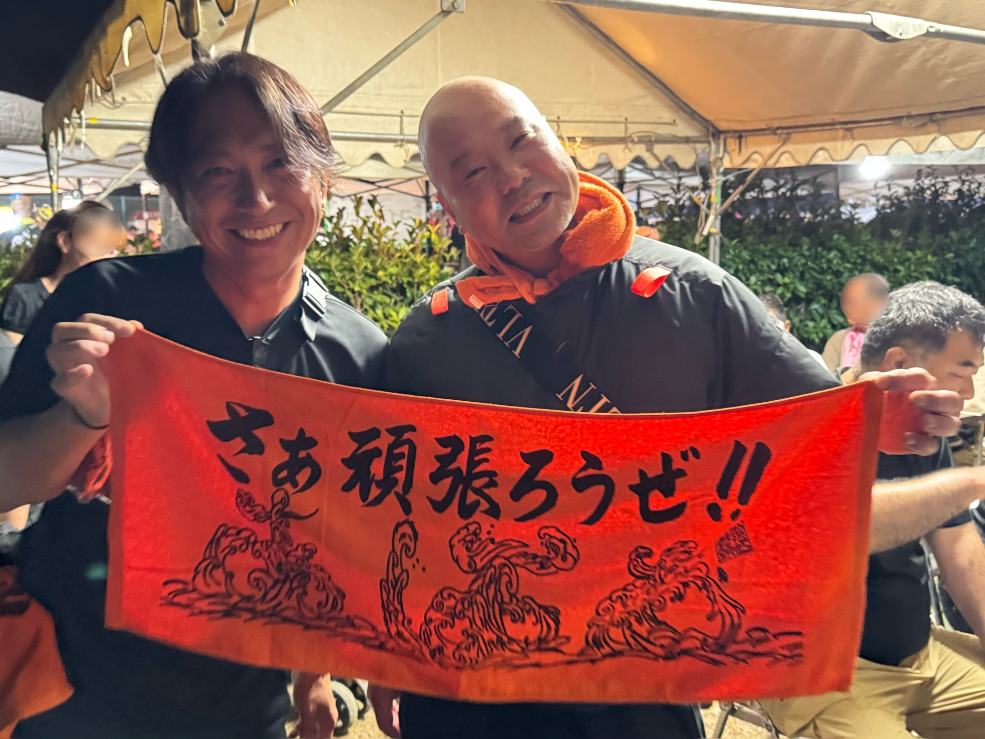 さぁ頑張ろうぜと書かれた橙色のタオルを2人で広げる